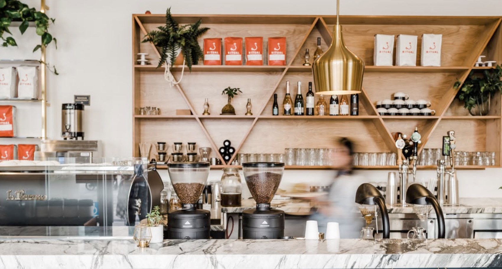 The marble counter with retail Ritual bags and wine bottles on the wood shelving behind